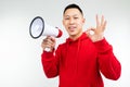 Studio portrait of a young Asian man in a red hoodie with a loudspeaker in his hands on a white background studio