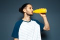 Studio portrait of young attractive guy, drinking water from reusable eco bottle, of yellow colour. Royalty Free Stock Photo