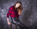 Studio portrait of young beautiful woman in a leather skirt sitting on high stool. Royalty Free Stock Photo