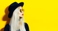 Studio portrait of young, beauty blonde girl wearing black hat and sunglasses. Looking away at empty background of yellow. Royalty Free Stock Photo
