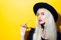 Studio portrait of young beauty blonde girl, wearing black shirt, round sunglasses, choker and hat on yellow background. Royalty Free Stock Photo