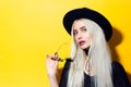 Studio portrait of young beauty blonde girl, wearing black shirt, round sunglasses, choker and hat on yellow background. Royalty Free Stock Photo