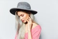 Studio portrait of young blonde cute girl listening the music via earbuds, on white background, wearing grey hat and pink shirt. Royalty Free Stock Photo