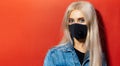 Studio portrait of young blonde girl with blue eyes wearing respiratory face mask against coronavirus. Background of red color.