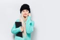 Studio portrait of young blonde girl holding laptop, using smartphone, wearing black hat and blue sweater on white background. Royalty Free Stock Photo