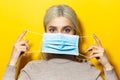 Studio portrait of a young blonde girl holding a medical flu mask on face, on yellow background. Royalty Free Stock Photo