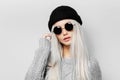 Studio portrait of young blonde girl wearing round sunglasses and black beanie hat on white background. Royalty Free Stock Photo