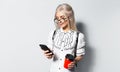 Studio portrait of young blonde teenager girl with paper cup of coffee takeaway in hand, looking in smartphone on white background Royalty Free Stock Photo