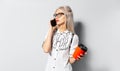 Studio portrait of young blonde teenager girl with paper cup of coffee takeaway in hand, talking on smartphone, on white Royalty Free Stock Photo