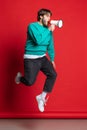 Full-length studio portrait of young boy jumping and shouting in megaphone isolated over red background Royalty Free Stock Photo