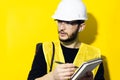 Studio portrait of young confident man, builder engineer writing in notebook, using wireless earphones, wearing safety helmet. Royalty Free Stock Photo