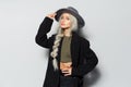 Studio portrait of young cute blonde girl with a braid, wearing black coat and grey hat, on white background. Royalty Free Stock Photo