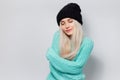 Studio portrait of young cute blonde girl embracing herself against white background. Wearing black hat and cyan sweater. Royalty Free Stock Photo