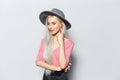 Studio portrait of young cute blonde girl with wireless earphones in ears, wearing grey hat and pink shirt, on white background. Royalty Free Stock Photo