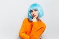 Studio portrait of young cute girl trying to be serious, on the background of white, wearing blue wig and orange sweater. Royalty Free Stock Photo