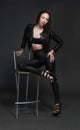 Portrait of a young dark-haired girl on a dark background sitting on a bar stool with dark leather pants, jacket and bra Royalty Free Stock Photo