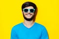 Studio portrait of young guy in blue shirt, wearing cyan sunglasses on background of yellow color. Royalty Free Stock Photo