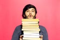 Studio portrait of young guy wearing round eyeglasses with bunch of books in hands on coral pink background.