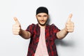 Studio portrait of young handsome man showing thumbs up on background of white, wearing red casual clothes and black head band. Royalty Free Stock Photo