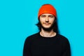 Studio portrait of young handsome man wearing orange hat and black sweater on blue background. Royalty Free Stock Photo