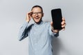 Studio portrait of young happy man showing the smartphone on white background. Wearing eyeglasses and blue shirt Royalty Free Stock Photo