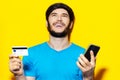 Studio portrait of young happy man using smartphone and credit card on background of yellow color. Royalty Free Stock Photo