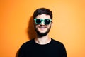 Studio portrait of young happy man, wearing aqua menthe or cyan sunglasses and black sweater on orange background. Royalty Free Stock Photo