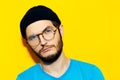 Studio portrait of young hipster guy wearing black beanie hat and round eyeglasses on background of yellow color. Royalty Free Stock Photo