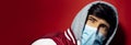 Studio portrait of young hooded man wearing medical flu mask against coronavirus on background of red color with copy space. Royalty Free Stock Photo