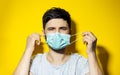 Studio portrait of young ill man, trying to put on, medical flu mask on yellow background. Royalty Free Stock Photo