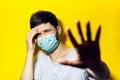 Studio portrait of young ill man who have headache, wearing medical flu mask, shows gesture STOP with hand on background of yellow Royalty Free Stock Photo