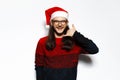 Studio portrait of young laughing man in red sweater, doing phone gesture, wearing Santa Claus hat and eyeglasses. Isolated on Royalty Free Stock Photo