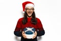 Studio portrait of young laughing man in red sweater, wearing Santa Claus hat and eyeglasses, holding blue round gift box in hands Royalty Free Stock Photo