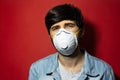 Studio portrait of young man in denim jacket, wearing respiratory medical flu mask against coronavirus on background of red color. Royalty Free Stock Photo