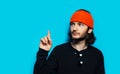 Studio portrait of young man pointing away against blue background. Wearing orange beanie hat and black sweater. Royalty Free Stock Photo