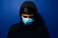 Studio portrait of young man, wearing medical flu mask and hooded sweater on background of dark blue color. Royalty Free Stock Photo