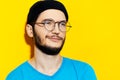 Studio portrait of young millennial wearing black beanie hat, round eyeglasses and cyan shirt on background of yellow color. Royalty Free Stock Photo