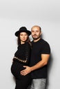 Studio portrait of young parents, pregnant woman wearing black hat and dress, man touching the belly on white background. Royalty Free Stock Photo