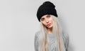 Studio portrait of young pretty blonde girl on background of white textured wall, wearing blue sweater and black hat. Royalty Free Stock Photo