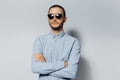 Studio portrait of young serious man with crossed arms, wearing sunglasses and blue shirt on white background Royalty Free Stock Photo