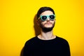 Studio portrait of young serious man wearing cyan sunglasses and black sweater on yellow background. Royalty Free Stock Photo