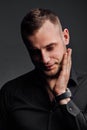 Studio portrait of young man in black shirt, holding hands in chin, looking down with humility. Royalty Free Stock Photo