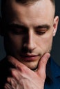 Studio portrait of young man in black shirt, holding hands in chin, looking down with humility. Royalty Free Stock Photo