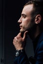 Studio portrait of young man in black shirt, holding hands in chin, looking down with humility. Royalty Free Stock Photo