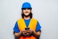 Studio portrait of young smiling construction worker engineer using smartphone against background of grey wall. Wearing safety. Royalty Free Stock Photo