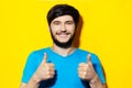 Studio portrait of young smiling guy in blue shirt showing thumbs up on background of yellow color. Royalty Free Stock Photo