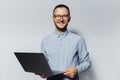 Studio portrait of young smiling guy holding a laptop in hands, wearing blue shirt and eyeglasses on white background Royalty Free Stock Photo