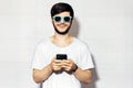 Studio portrait of young smiling guy with smartphone in hands, wearing cyan shades, background of white color. Royalty Free Stock Photo