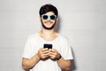 Studio portrait of young smiling guy with smartphone in hands, wearing cyan shades, background of white color. Royalty Free Stock Photo