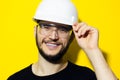 Studio portrait of young smiling man architect, builder engineer, wearing black sweater, touching his white construction safety he Royalty Free Stock Photo